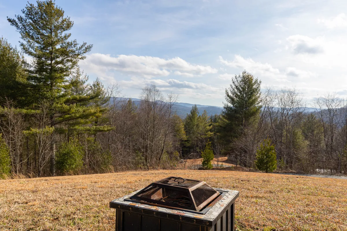 This exterior shot captures a cozy fire pit surrounded by chairs, with distant mountains and trees in the background. The open sky and natural landscape create a welcoming setting for outdoor gatherings, storytelling around the fire, and stargazing.