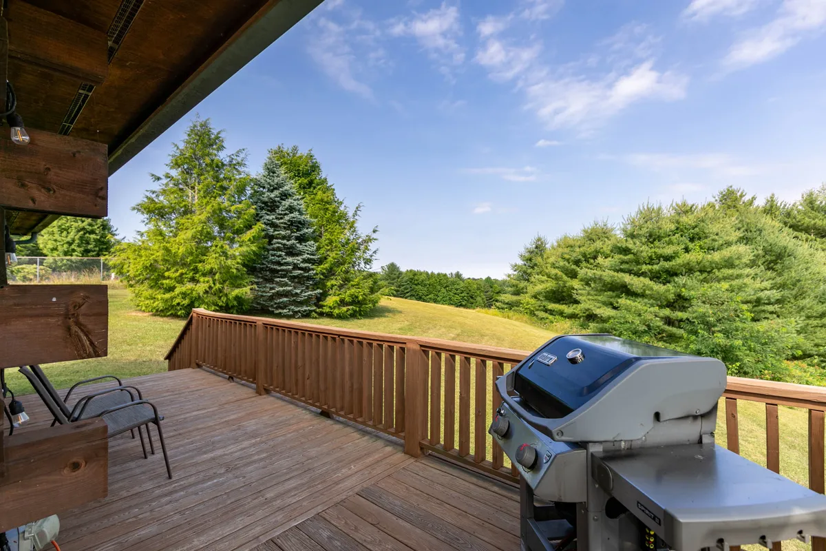 The image shows a spacious wooden deck with a railing, grill, and seating area, surrounded by lush trees. The deck is set up for barbecuing and outdoor dining, inviting families to enjoy meals together while immersed in nature. The tranquil setting is perfect for unwinding after a day of nearby park adventures.