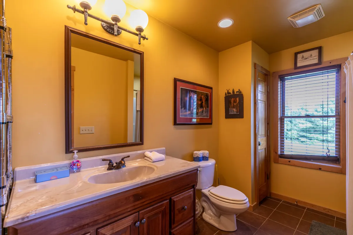 A bright and welcoming bathroom with a mirror, sink, window, and tasteful artwork. Natural light fills the space, creating a refreshing setting ideal for morning or evening routines.