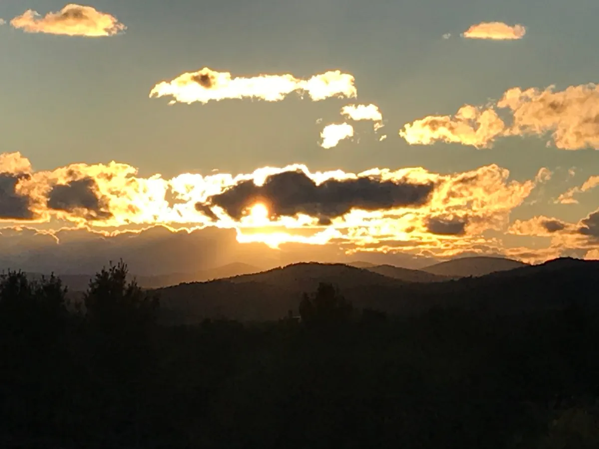 A spectacular sunset scene where the sky is awash with warm colors over layers of mountain silhouettes and dramatic cloud formations. The setting feels tranquil and intimate, ideal for quiet reflection or sharing a serene moment with a loved one. No structures are visible—just nature’s grandeur in full display.