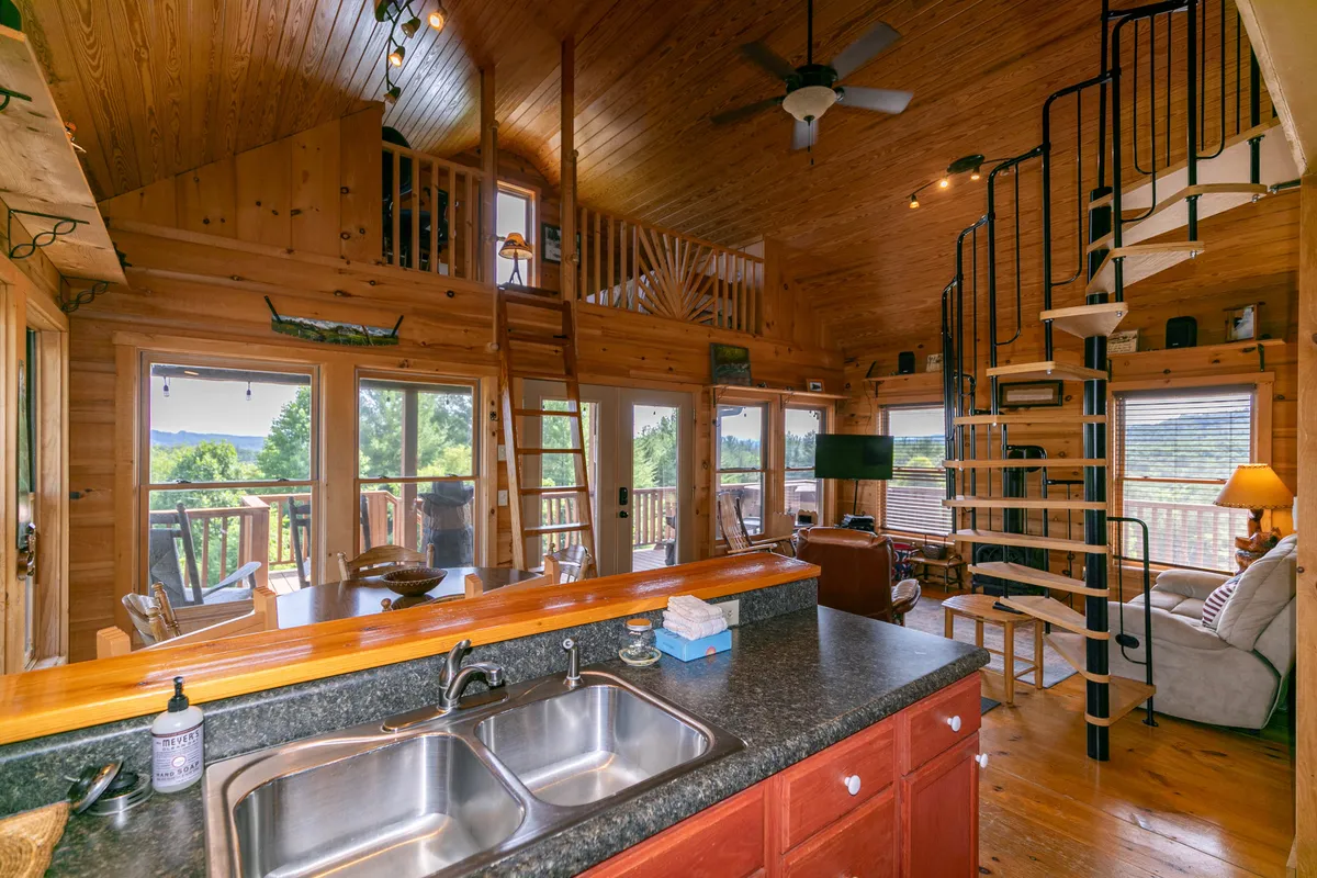A wide view of the kitchen area highlighted by a kitchen island, wooden ceiling, spiral staircase, and large windows. The space invites both cooking and socializing, with open sightlines that make it easy for guests to gather and interact.