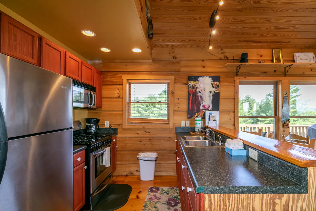 A warmly lit kitchen featuring stainless steel appliances, sleek wooden cabinetry, and a kitchen island. Natural light streams in through a window, and the layout offers ample counter space and modern amenities. The overall feel is both functional and inviting, ideal for cooking and gathering.