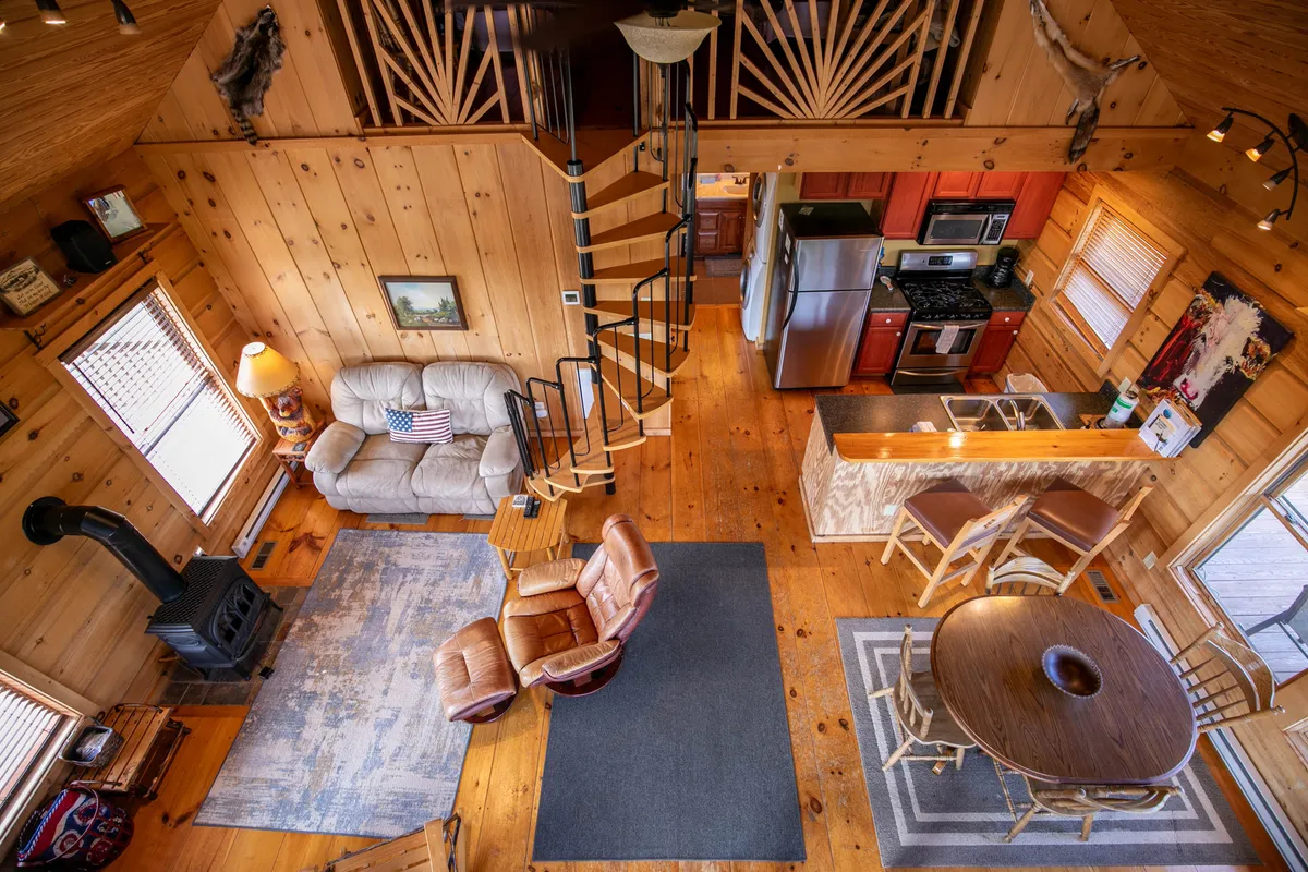 A comfortable living area showcasing a spiral staircase leading to the loft, a cushy couch, a wooden dining table, and a wood-burning stove. The spiral staircase stands out as a unique architectural feature, while the room radiates warmth and togetherness.