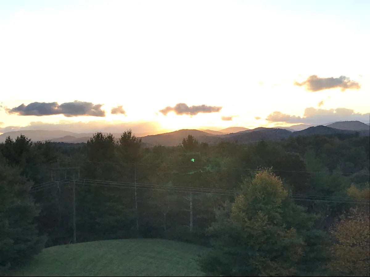 A wide, serene view of the mountains at sunset, with a glowing sky above a tree-lined horizon. The tranquil scene invites guests to relax, take nature walks, and watch the sun fade into a night perfect for stargazing.