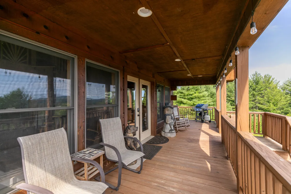 A welcoming exterior scene featuring rocking chairs and a grill on the deck, with the deck railing framing a scenic outdoor view. The setup evokes relaxation and socializing, inviting guests to enjoy morning coffee or sunset grilling in comfort while surrounded by greenery and natural beauty.